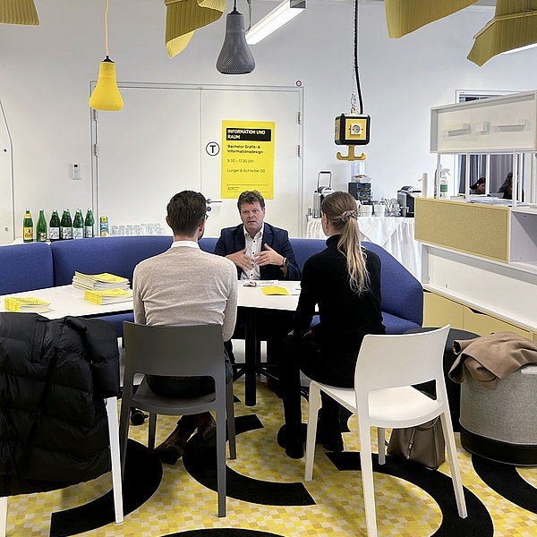 3 Personen bei einem Tisch sprechen miteinander