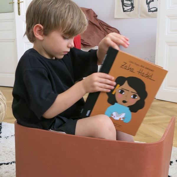 Ein Kind, das auf einem Prototypen "Ludo" sitzt und mit einem Buch spielt