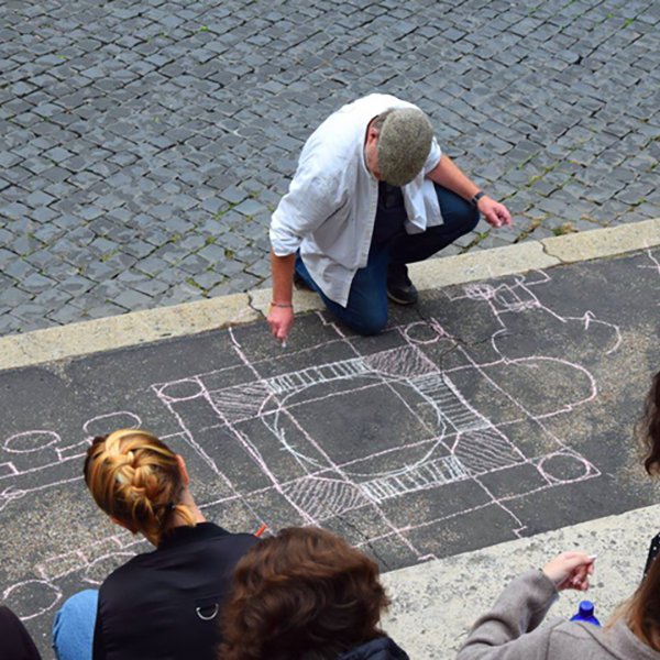 Eine Person kniet am Boden und zeichnet mit Kreide auf den Asphalt