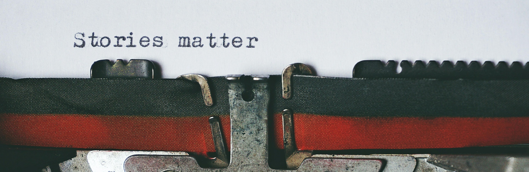 Eine alte Schreibmaschine auf weißem Hintergrund in die ein Papier eingeschoben ist auf dem steht "Storys matter"