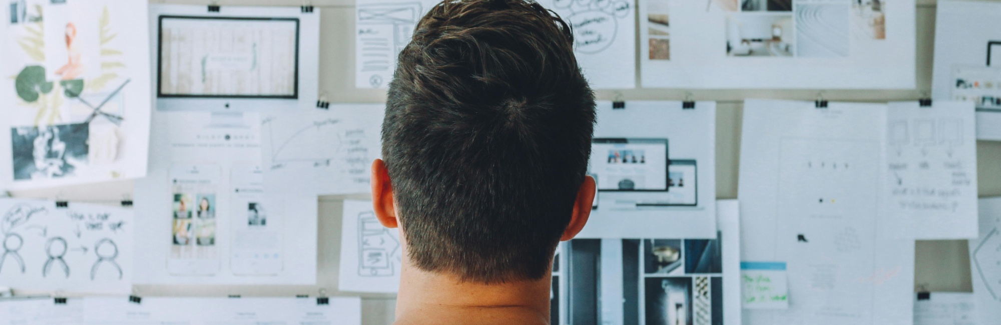 Wand mit vielen aufgeh&auml;ngten Papieren, auf denen verschiedene Zeichnungen und Ideen zu sehen sind, der Kopf eines Mannes ist davor zu sehen