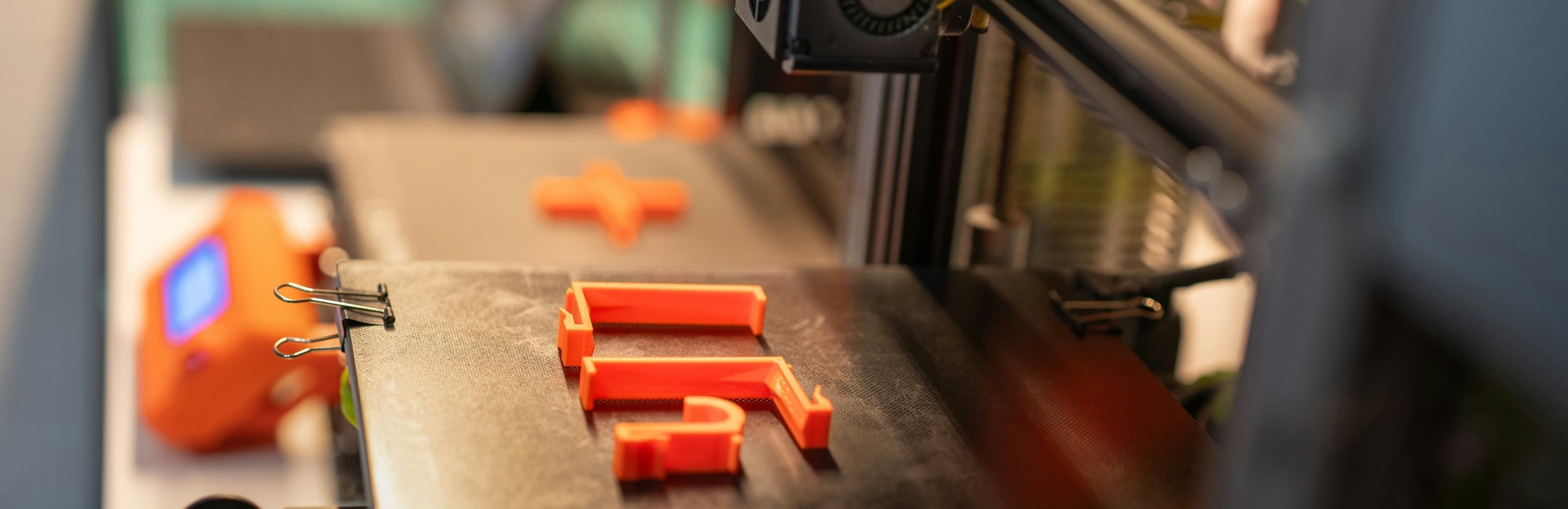 Das Bid zeigt den Ausschnitt eines 3D-Druckers der ein neon-orangenes Modell druckt